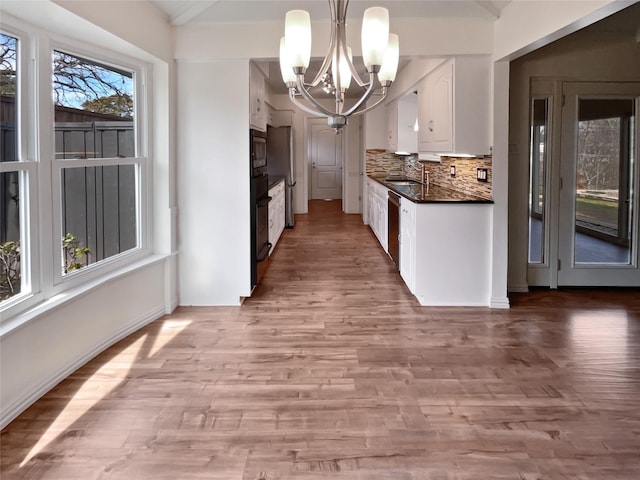 kitchen featuring white cabinetry, sink, backsplash, hanging light fixtures, and light wood-type flooring