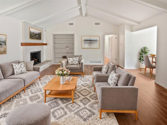 living room featuring a fireplace, built in shelves, light hardwood / wood-style flooring, and lofted ceiling with beams