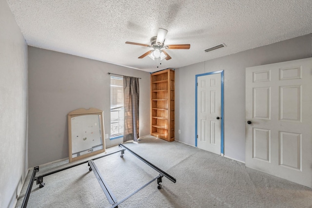 workout room featuring ceiling fan, light colored carpet, and a textured ceiling