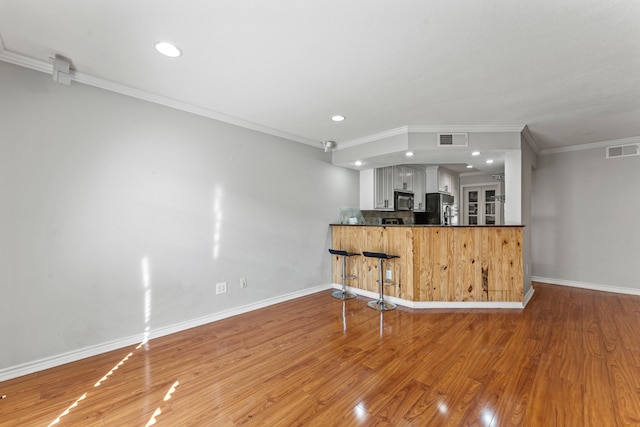 kitchen with black refrigerator, hardwood / wood-style floors, white cabinets, kitchen peninsula, and crown molding