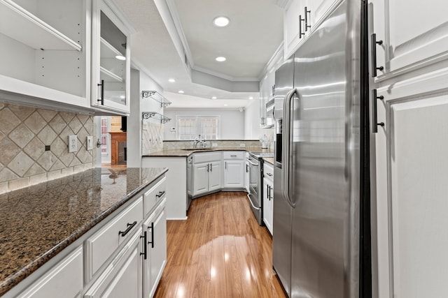 kitchen featuring crown molding, white cabinetry, dark stone countertops, stainless steel appliances, and decorative backsplash