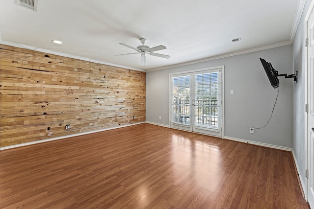 empty room with crown molding, wood walls, ceiling fan, and hardwood / wood-style flooring