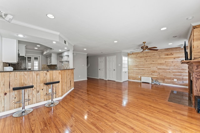 interior space featuring a kitchen breakfast bar, wooden walls, kitchen peninsula, light hardwood / wood-style floors, and white cabinets