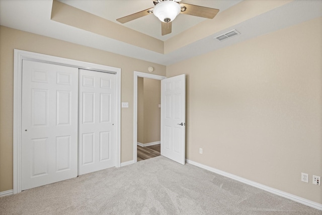 unfurnished bedroom featuring ceiling fan, a raised ceiling, carpet floors, and a closet