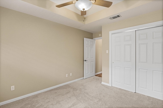 unfurnished bedroom with light carpet, a tray ceiling, a closet, and ceiling fan