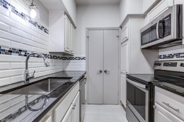 kitchen featuring dark stone countertops, stainless steel appliances, sink, and white cabinets