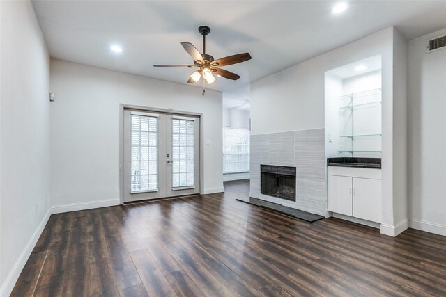 unfurnished living room featuring dark wood-type flooring, ceiling fan, a tile fireplace, and french doors