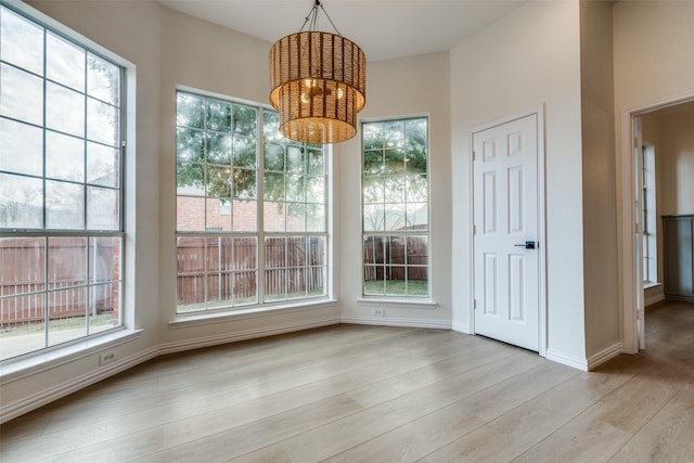 unfurnished dining area featuring a healthy amount of sunlight, a notable chandelier, and light hardwood / wood-style floors