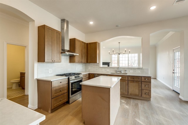 kitchen with a kitchen island, sink, hanging light fixtures, gas stove, and wall chimney range hood