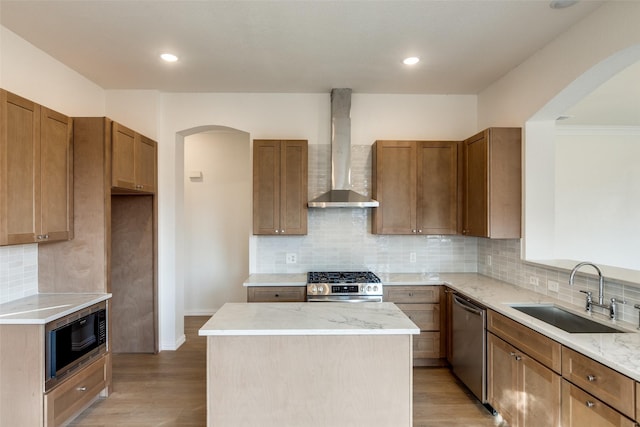 kitchen with sink, a center island, stainless steel appliances, light wood-type flooring, and wall chimney exhaust hood