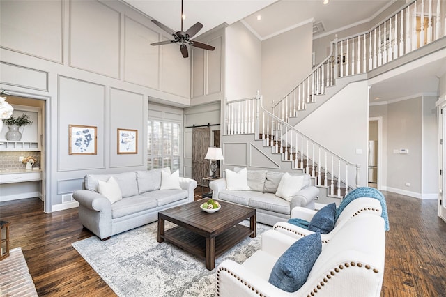 living room featuring dark hardwood / wood-style floors, a high ceiling, ceiling fan, crown molding, and a barn door