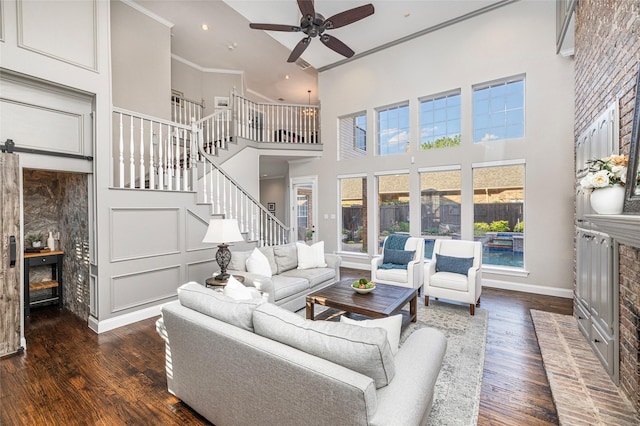 living room with a towering ceiling, dark hardwood / wood-style floors, ceiling fan, crown molding, and a brick fireplace