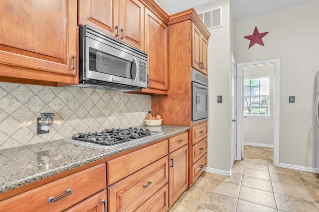 kitchen with stainless steel appliances, tasteful backsplash, light tile patterned flooring, and light stone counters