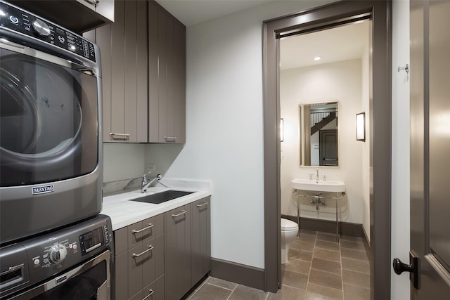 clothes washing area featuring sink, cabinets, stacked washer and clothes dryer, and dark tile patterned flooring