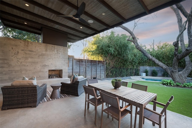 patio terrace at dusk featuring ceiling fan, outdoor lounge area, and a lawn