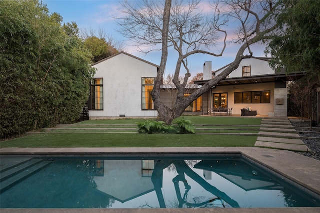 back house at dusk featuring a yard, a patio area, and ceiling fan