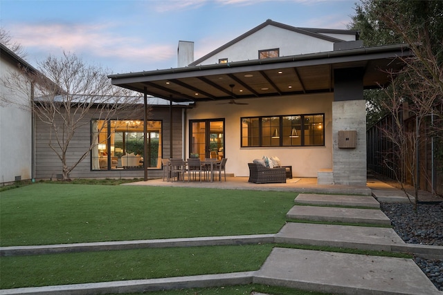 back house at dusk featuring a yard, a patio area, outdoor lounge area, and ceiling fan