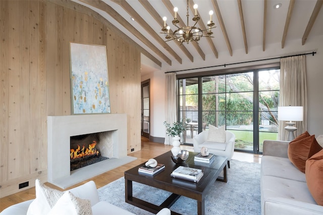 living room featuring a premium fireplace, beam ceiling, light hardwood / wood-style flooring, and a notable chandelier