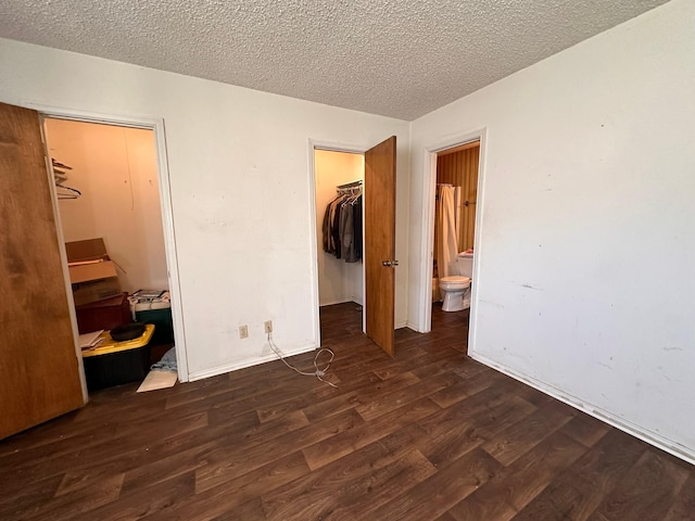 unfurnished bedroom with dark hardwood / wood-style floors, ensuite bathroom, a textured ceiling, a spacious closet, and a closet