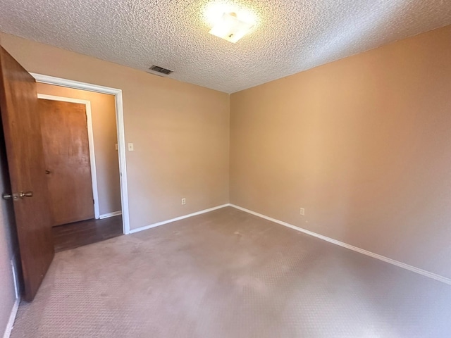 empty room with carpet flooring, a textured ceiling, baseboards, and visible vents