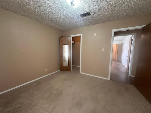 unfurnished bedroom featuring carpet floors, a spacious closet, a textured ceiling, baseboards, and visible vents