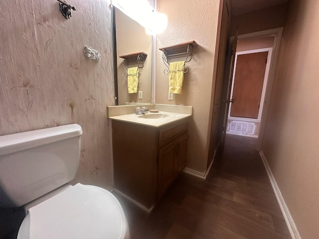 bathroom featuring vanity, toilet, a textured wall, baseboards, and wood finished floors