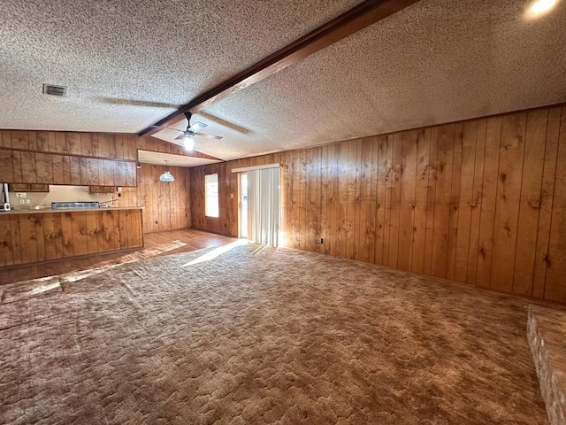 unfurnished living room featuring vaulted ceiling with beams, carpet floors, a textured ceiling, and wood walls