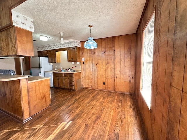 kitchen featuring pendant lighting, wooden walls, dark hardwood / wood-style flooring, white appliances, and a textured ceiling