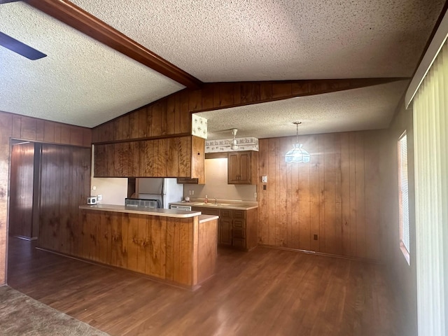 kitchen featuring freestanding refrigerator, lofted ceiling with beams, a peninsula, brown cabinets, and dark wood-style flooring