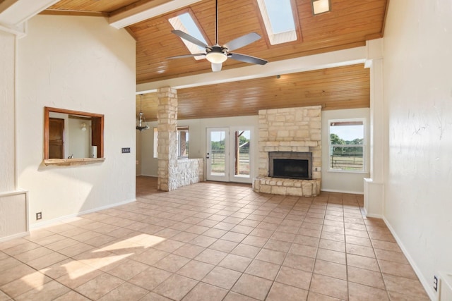 unfurnished living room featuring light tile patterned floors, beam ceiling, a skylight, a stone fireplace, and wooden ceiling