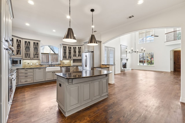 kitchen with visible vents, arched walkways, appliances with stainless steel finishes, a center island, and a sink