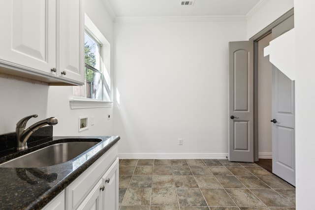 kitchen featuring baseboards, dark stone countertops, crown molding, white cabinetry, and a sink