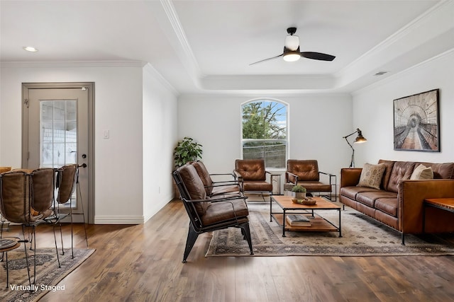 living room featuring a raised ceiling, ornamental molding, wood finished floors, and a wealth of natural light