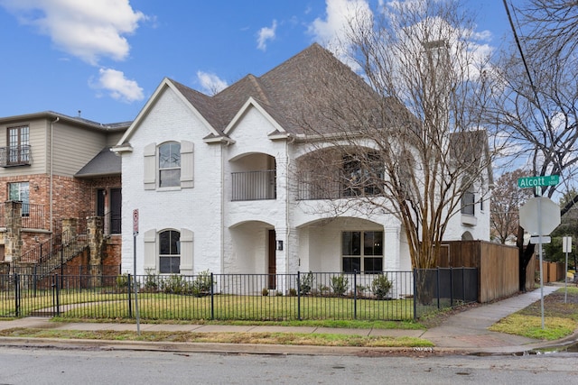 french provincial home featuring a fenced front yard, brick siding, a front lawn, and roof with shingles