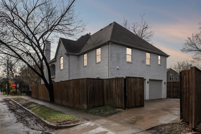 view of home's exterior with an attached garage, brick siding, a shingled roof, fence, and concrete driveway