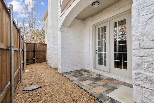 view of exterior entry featuring brick siding, fence, and a patio