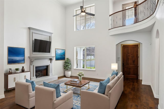 living room featuring arched walkways, a fireplace with raised hearth, baseboards, and wood finished floors