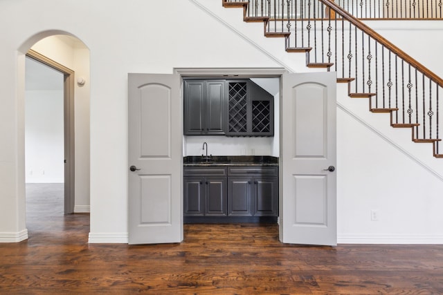 bar featuring arched walkways, dark wood-type flooring, a sink, stairway, and wet bar