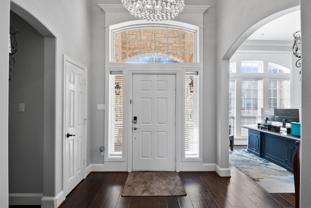 entryway with dark hardwood / wood-style flooring, a towering ceiling, ornamental molding, and a chandelier