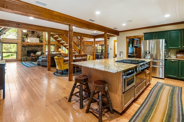 kitchen featuring beamed ceiling, appliances with stainless steel finishes, light stone countertops, and a kitchen island