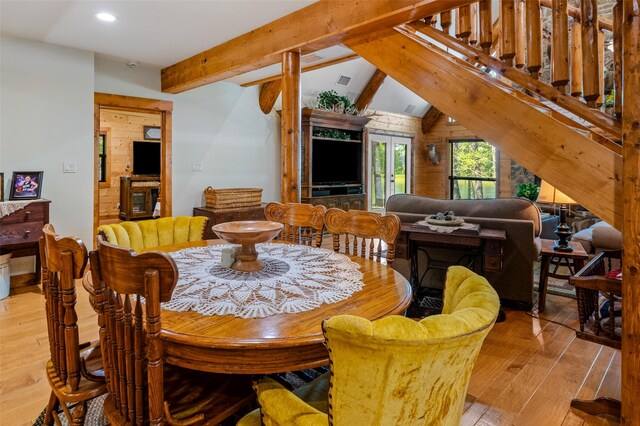 dining area featuring vaulted ceiling with beams, wood walls, and light hardwood / wood-style flooring