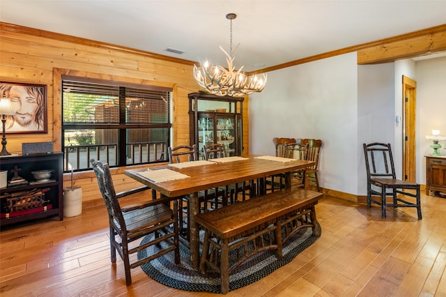 dining room with an inviting chandelier, crown molding, wooden walls, and light wood-type flooring