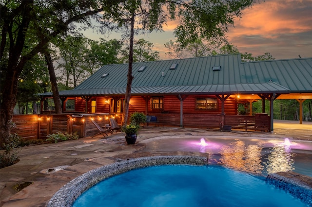 pool at dusk with a gazebo, pool water feature, and a patio area