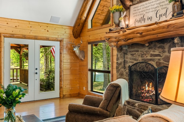 interior space featuring a fireplace, wooden walls, french doors, lofted ceiling, and light hardwood / wood-style flooring