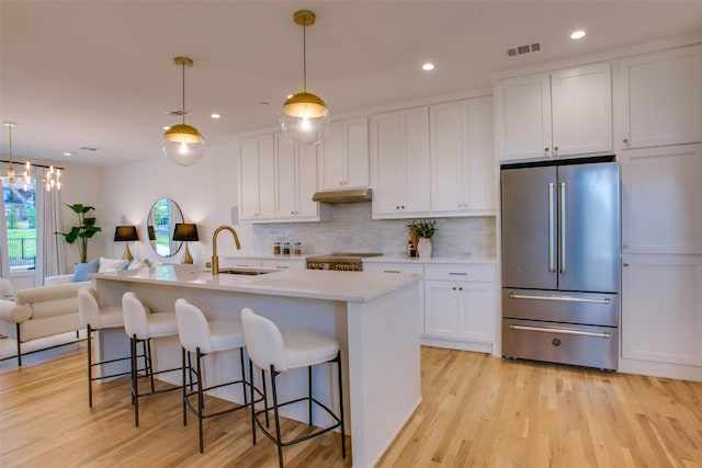 kitchen with hanging light fixtures, a center island with sink, high quality fridge, and sink