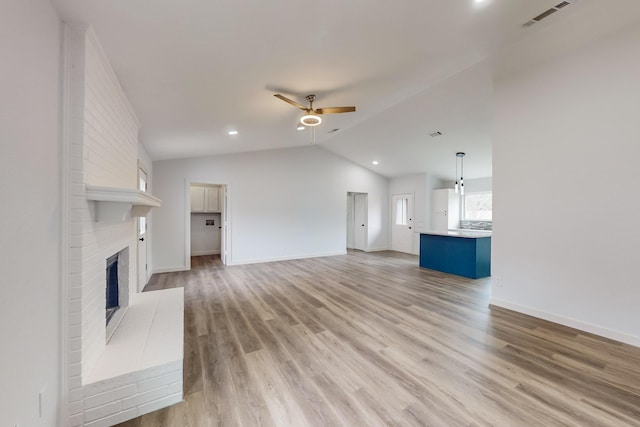 unfurnished living room featuring ceiling fan, lofted ceiling, a brick fireplace, and light wood-type flooring