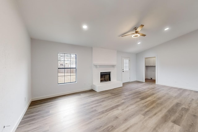 unfurnished living room featuring ceiling fan, plenty of natural light, a brick fireplace, and light hardwood / wood-style flooring