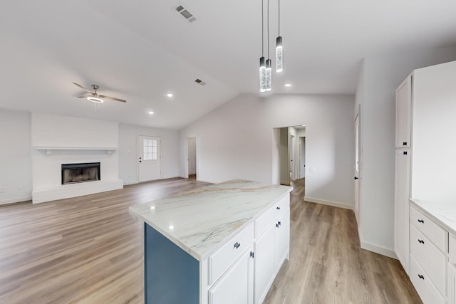 kitchen featuring light stone counters, white cabinetry, a brick fireplace, hanging light fixtures, and a kitchen island