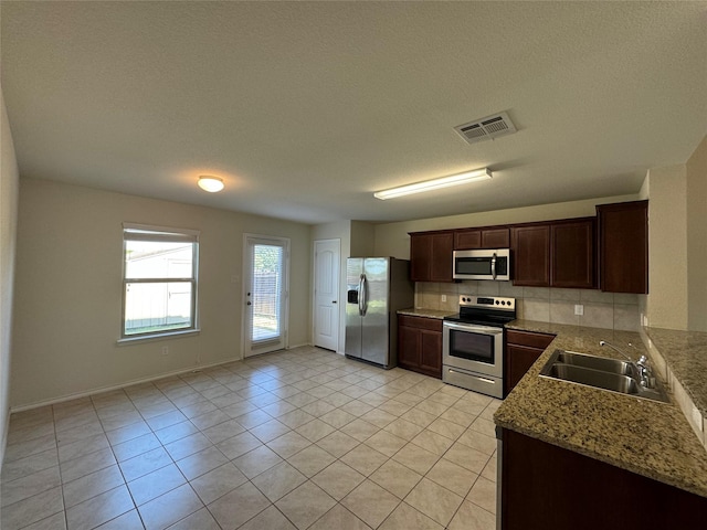 kitchen with dark brown cabinetry, sink, tasteful backsplash, light stone counters, and stainless steel appliances