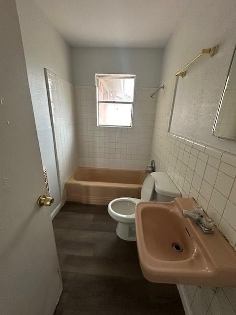 full bathroom with wood-type flooring, sink, tile walls, tiled shower / bath combo, and toilet